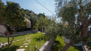A garden with a stone pathway, a wooden fence, and a large tree. - Il Sole di Poggi (Imperia)