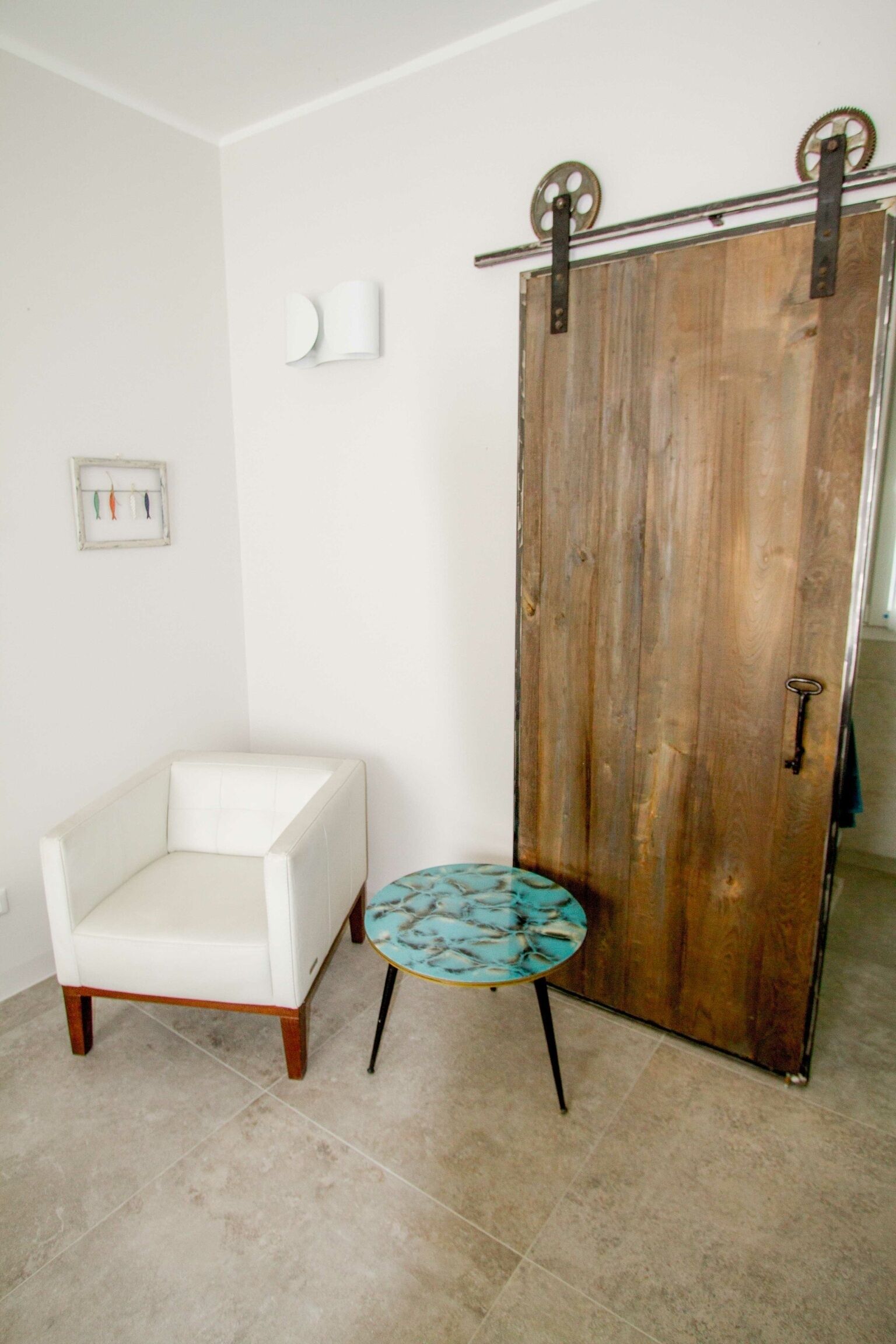 Une pièce comprenant un fauteuil blanc, une petite table ronde à motifs bleus et blancs, et une porte en bois avec des ferrures métalliques.