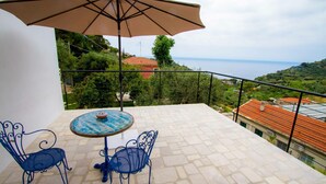A balcony with a table and chairs, a large umbrella, and a scenic view of the sea and hills. - Il Sole di Poggi (Imperia)