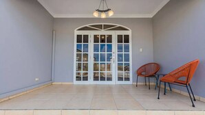 Een ruime patio met betegelde vloer, een witte boogdeur en twee oranje stoelen.