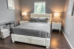 Une chambre à coucher avec un lit, deux tables de chevet, une commode, une petite chaise blanche et une fenêtre.