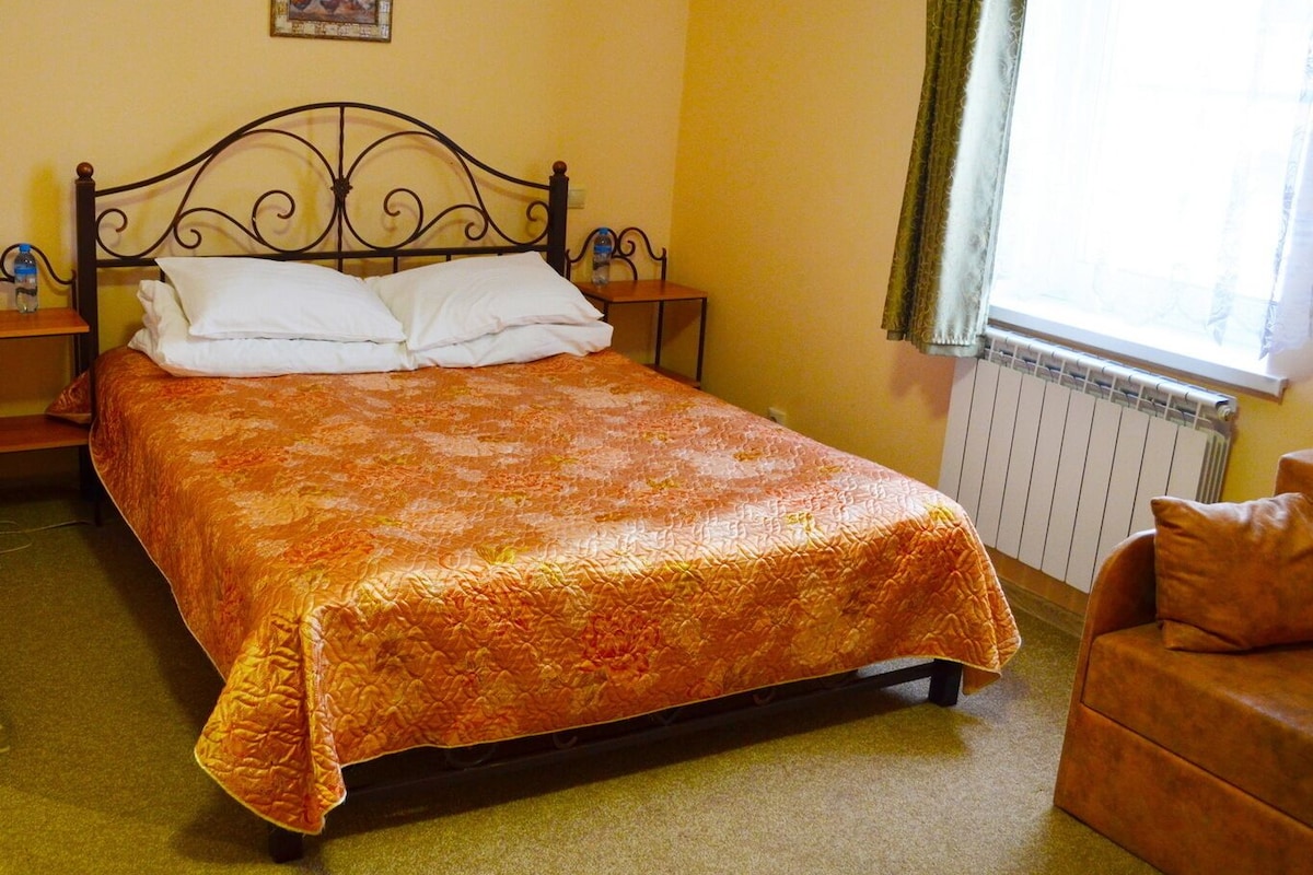 Una cama bien hecha con una colcha estampada, un cabecero de madera y una mesita de noche con una botella.
