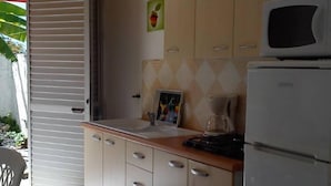 A compact kitchen with wooden cabinets, a microwave, and a refrigerator. - Sun, sea and easy living in this studio close to everything (SAINT FRANCOIS)