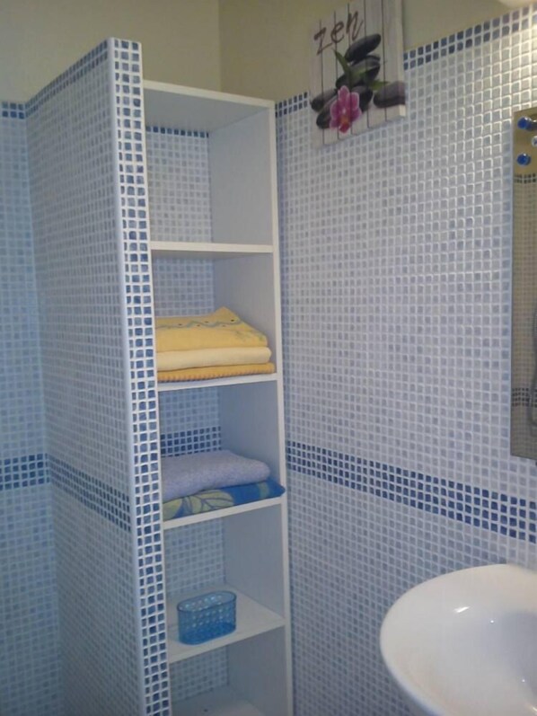 Ein Badezimmer mit einem weißen Waschbecken, einer blau-weißen Fliesenwand und einem Regal mit gefalteten Handtüchern.