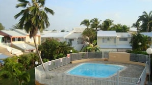 A swimming pool surrounded by a white fence, with palm trees and houses in the background. - Sun, sea and easy living in this studio close to everything (SAINT FRANCOIS)