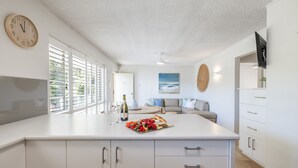 A modern kitchen with a central island, white cabinetry, and a large window with blinds. - Shoal Court 4, 7 Lillian St - water views , linen, bed making (Shoal Bay)