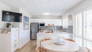 A modern kitchen with white cabinetry, a built-in oven, and a dining area with a round table. - Shoal Court 4, 7 Lillian St - water views , linen, bed making (Shoal Bay)