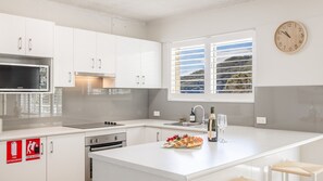 A modern kitchen with white cabinets, a stainless steel microwave, a built-in oven, and a large window with a view of the countryside.