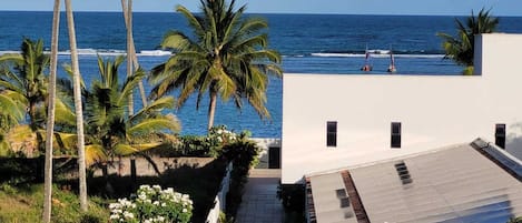 A modern building with a flat roof, a paved patio, and a view of the ocean.