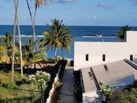 Un edificio moderno con techo plano, un patio empavedado y vista al océano.