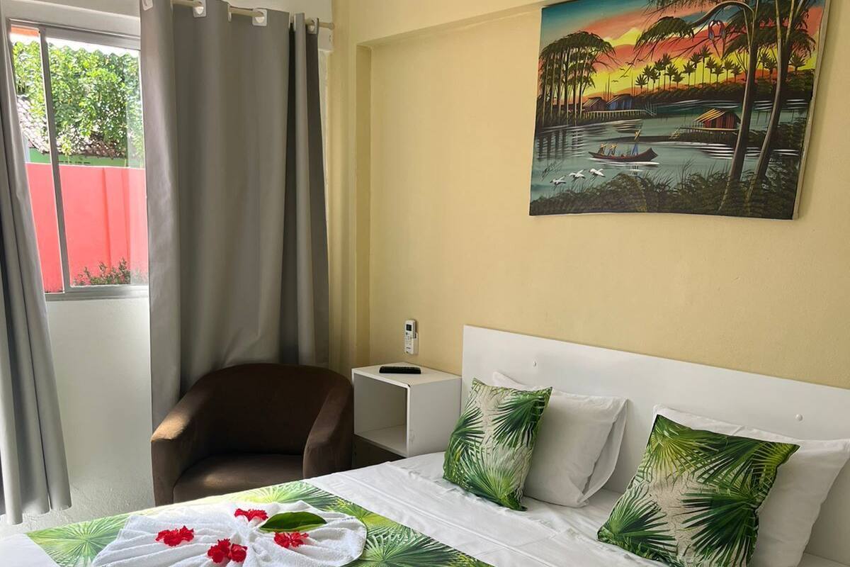 Habitación de hotel con cama, una silla, una mesita de noche, un cuadro y vistas al verdor exterior.