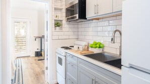 Una cocina moderna con armarios blancos, una campana extractora negra, un lavamanos de acero inoxidable y una encimera con tabla de cortar y manzanas.