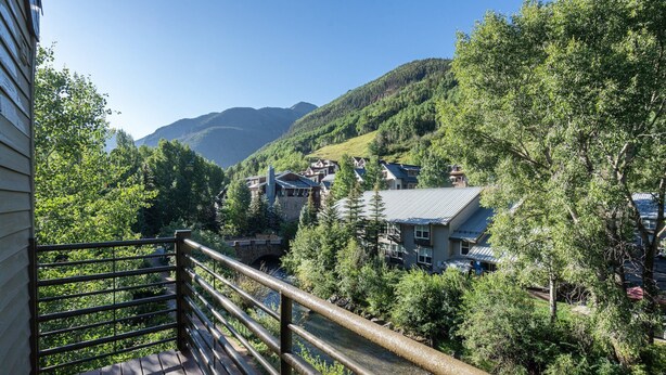 Una terraza de madera con barandilla de metal que da a un valle con casas y árboles.