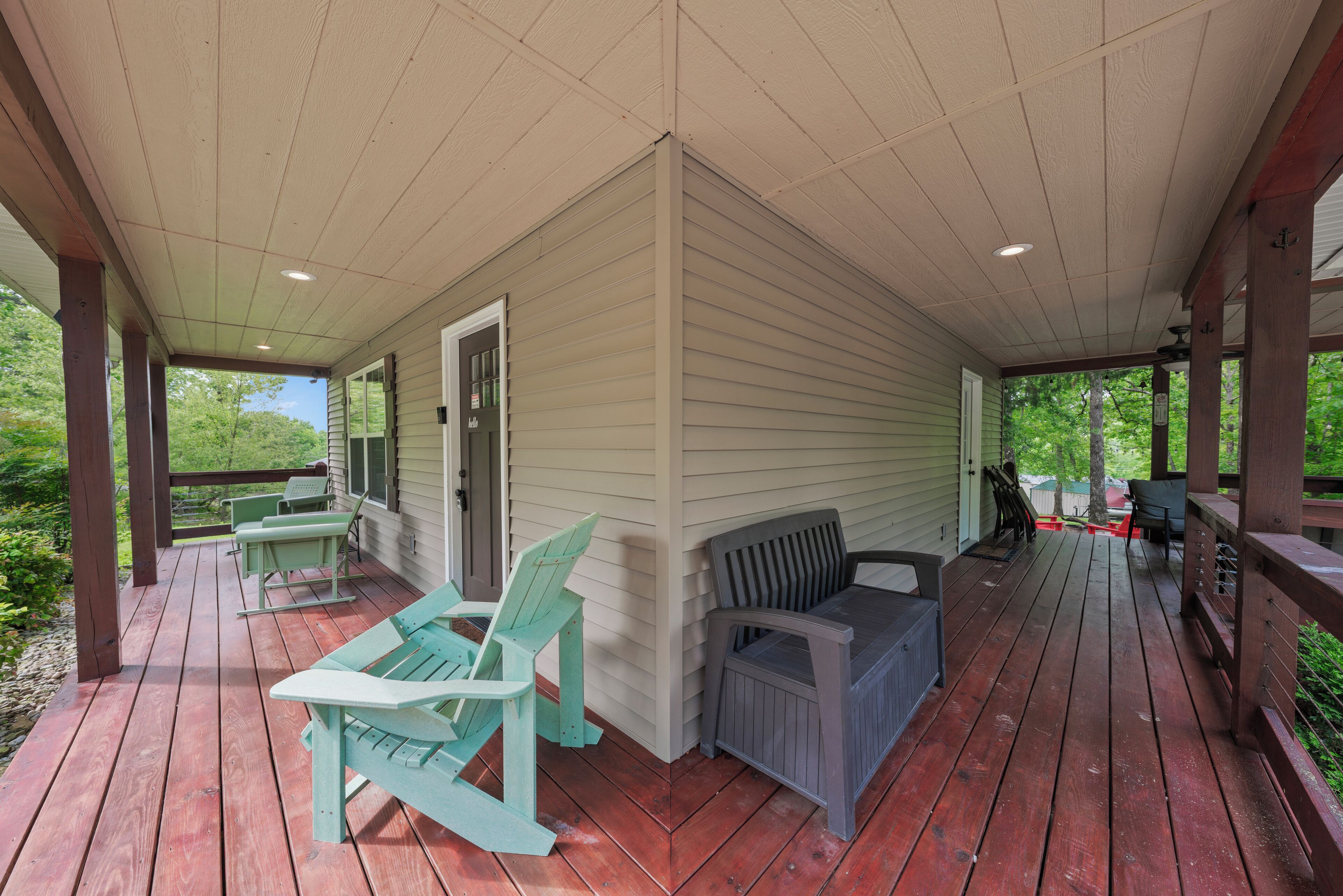 A covered porch with wooden flooring, two Adirondack chairs, a gray sofa, and a small table.