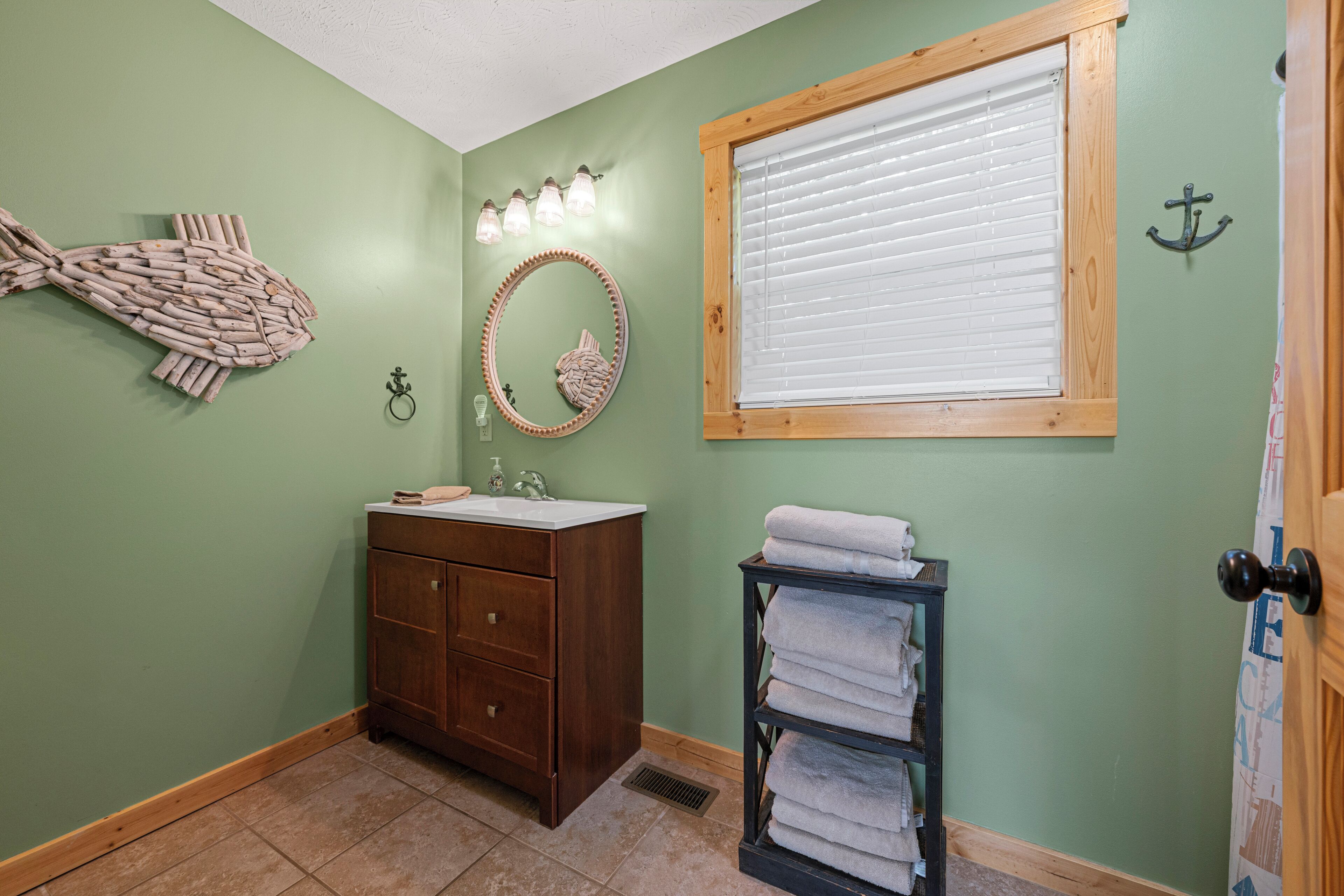 A bathroom with a wooden vanity, a round mirror, a towel rack, and a fish wall decoration.