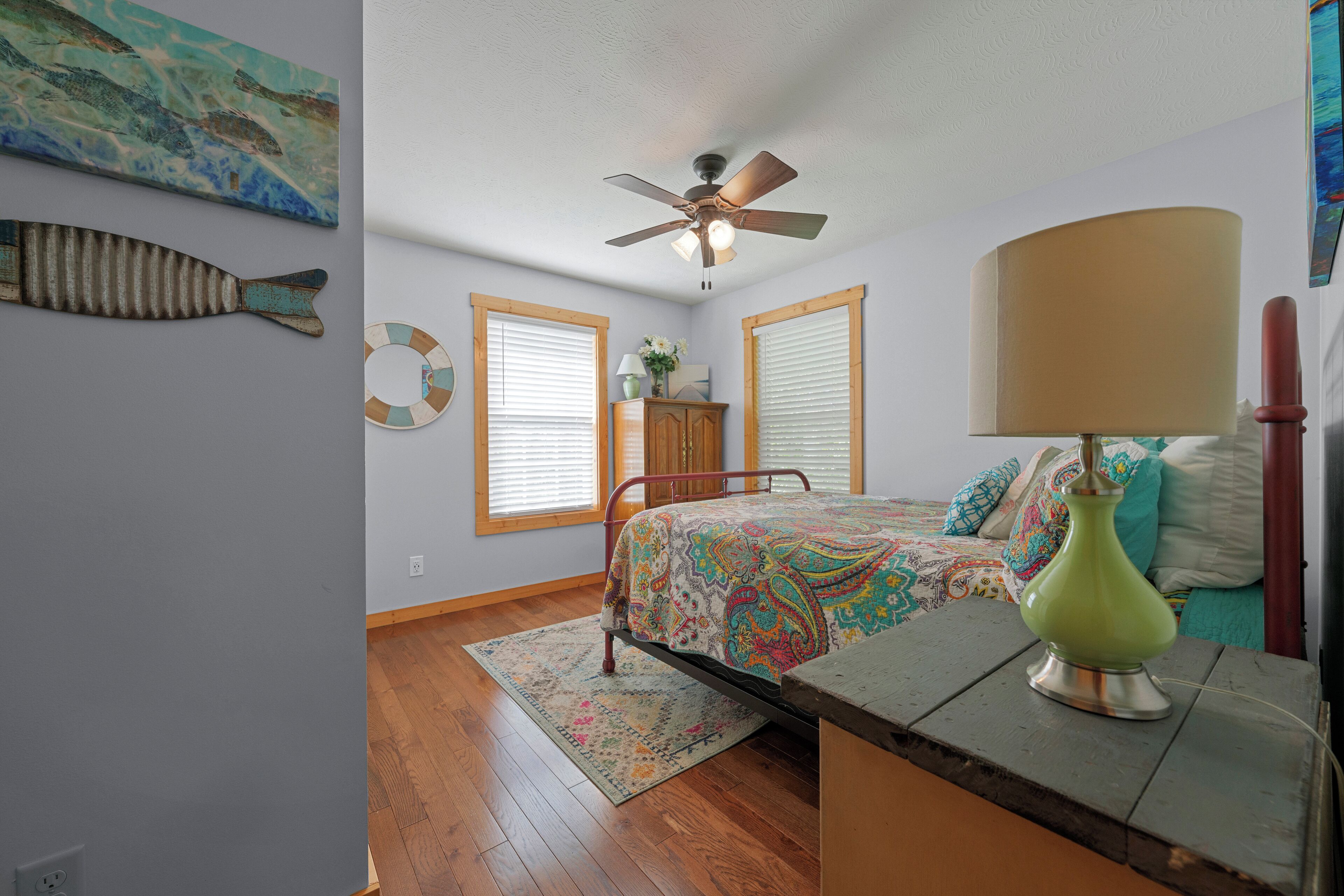 Un dormitorio con cama, ventilador de techo, lámpara y una decoración de peces en la pared.