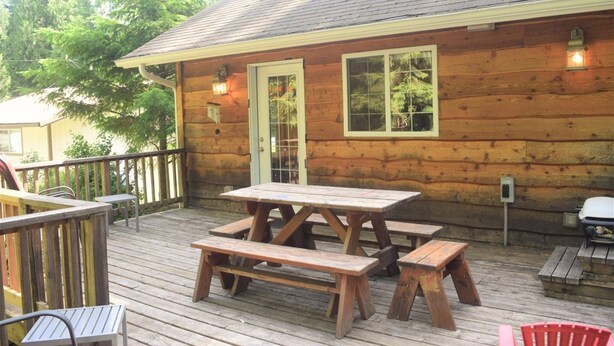 Una cabaña de madera con terraza, mesa de picnic y bancos.