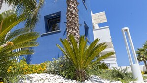 Un edificio de fachada azul, con palmeras y flores amarillas al frente.