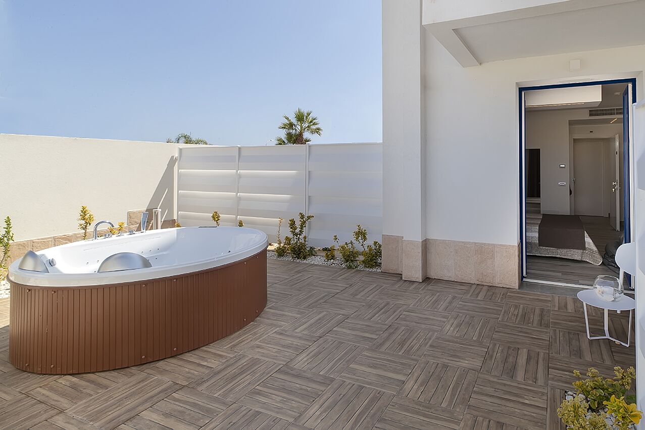 Un espacio exterior moderno con un jacuzzi de madera, una mesita con una copa y una puerta que da a un espacio interior.