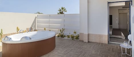 Un espacio exterior moderno con un jacuzzi de madera, una mesita con una copa y una puerta que da a un espacio interior.