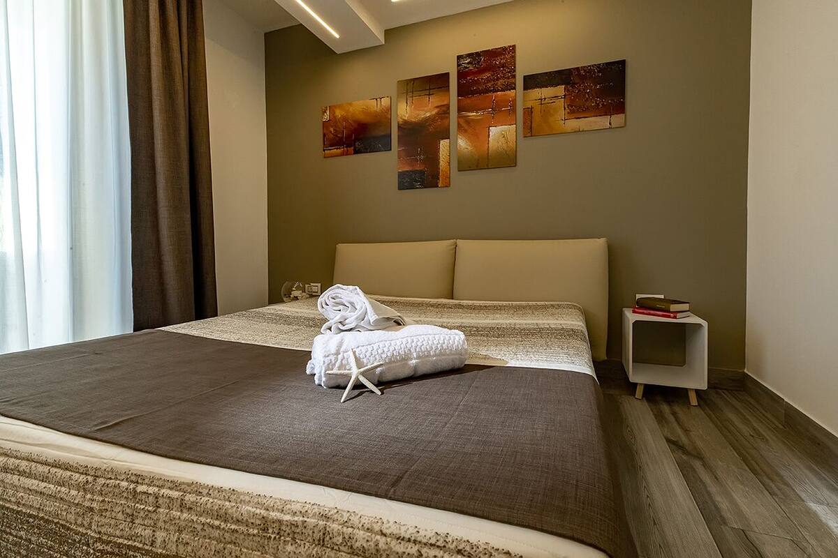 Quarto de hotel com uma cama grande, uma mesa de cabeceira e uma parede com três quadros.