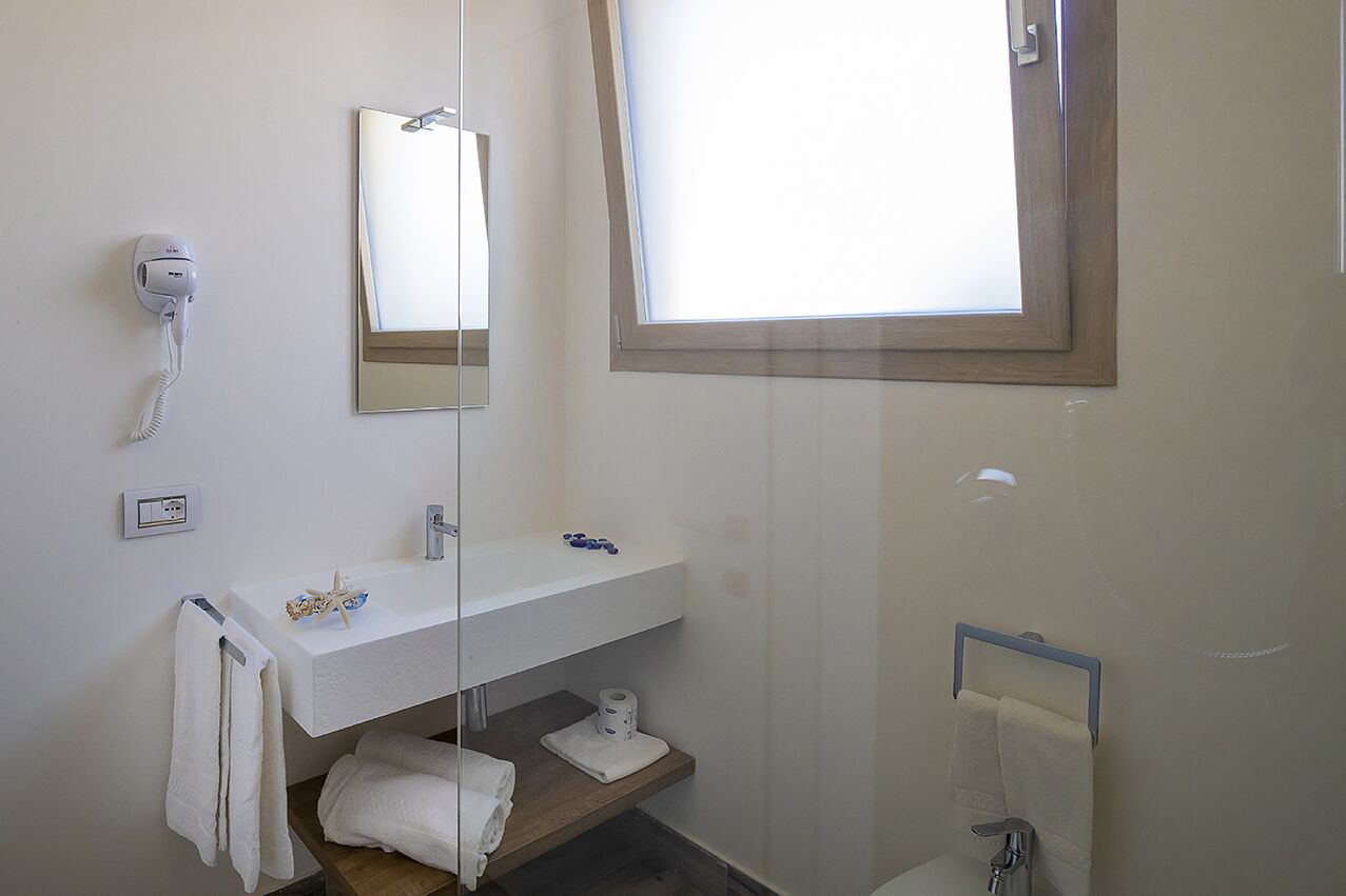 Un baño con lavamanos blanco, un espejo, un secador de pelo, un perchero para toallas y una ventana.