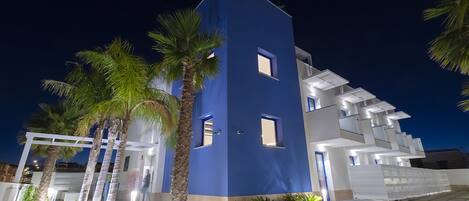 Un edificio moderno con fachada azul, balcones blancos y un patio con baldosas y palmeras.
