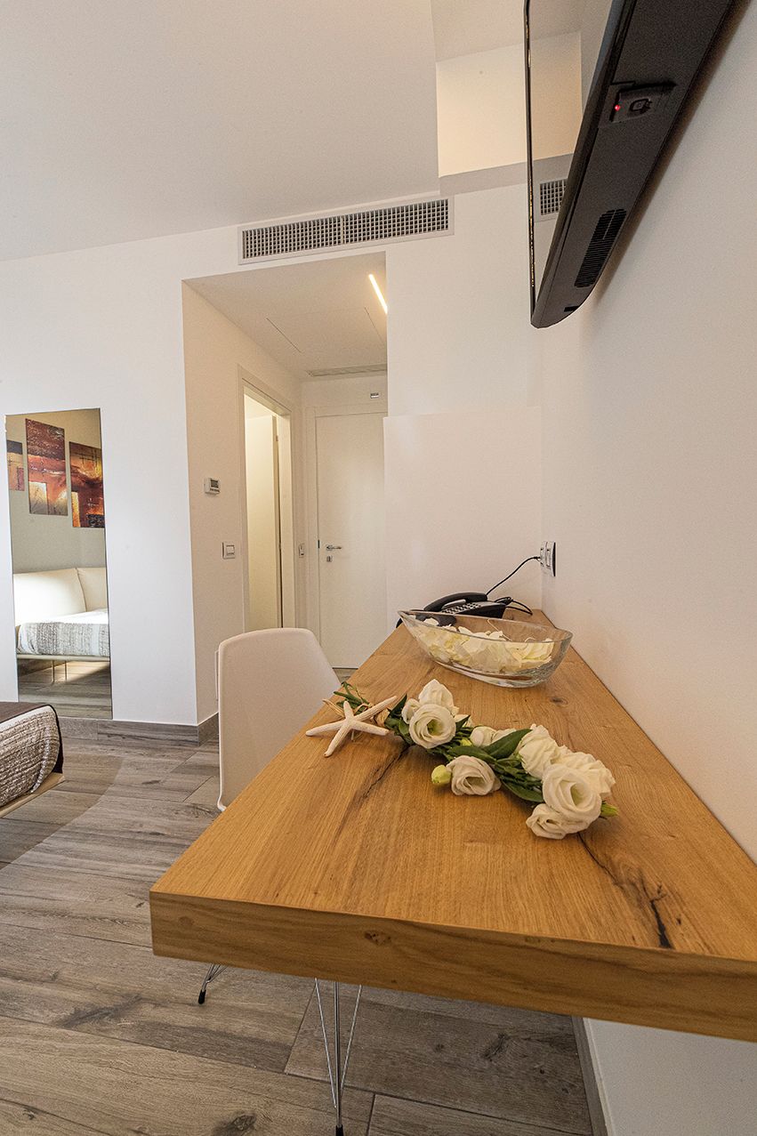 A modern room with a wooden dining table, a clear glass bowl with white flowers, and a telephone on the wall.