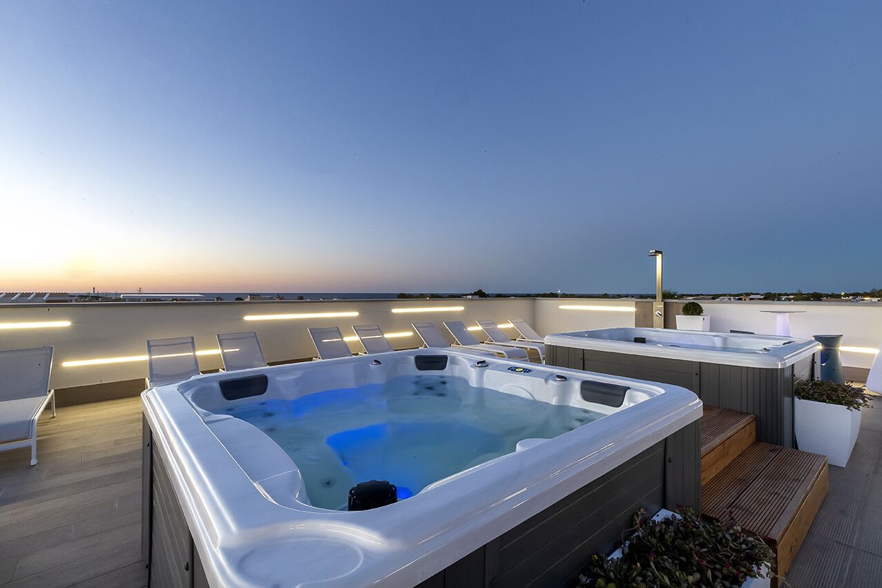 A rooftop terrace with multiple hot tubs and lounge chairs, overlooking a body of water.