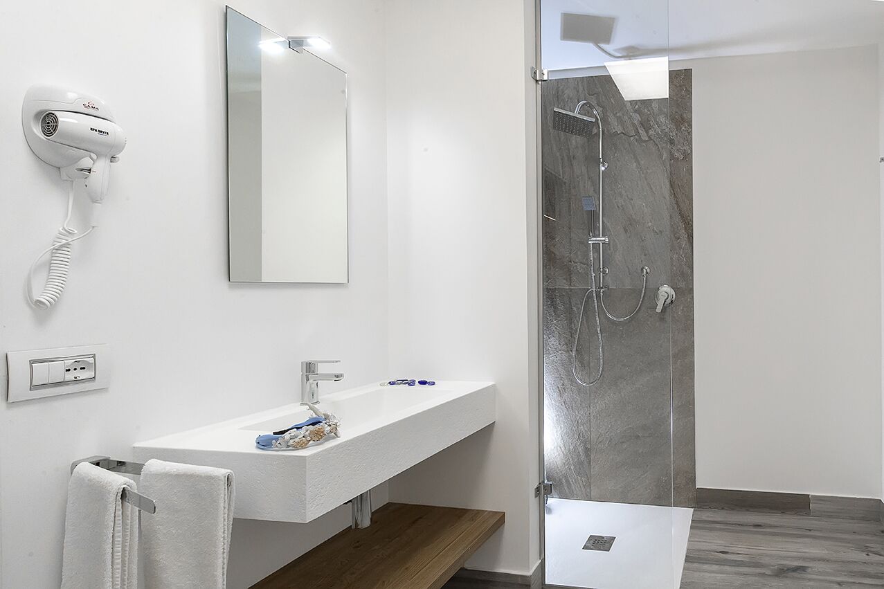 A modern bathroom with a white sink, a mirror, a hair dryer, and a shower with a marble wall.