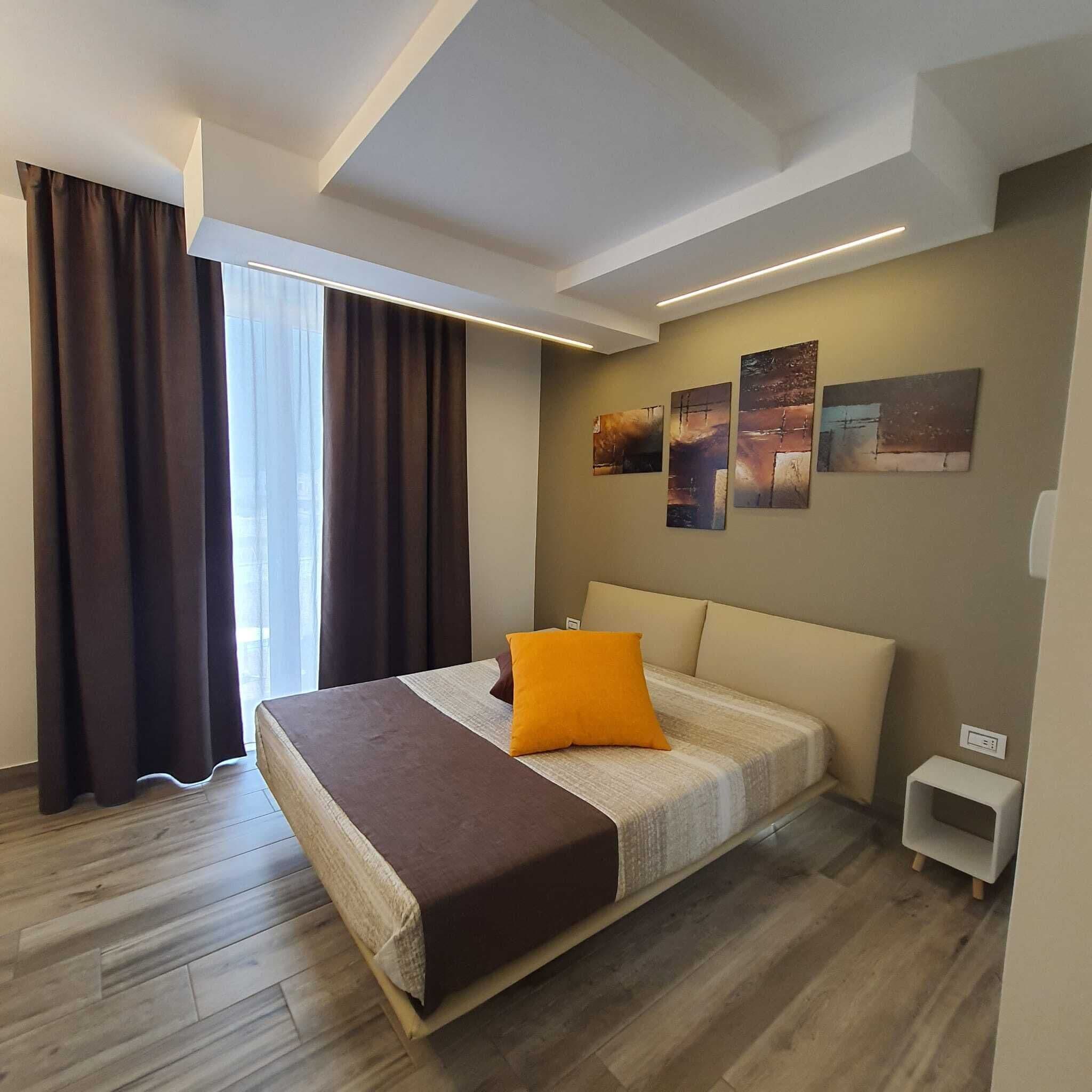 A modern bedroom with a large bed, a small bedside table, and three wall-mounted artworks.