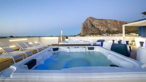 Área de piscina en la azotea con sillones de descanso y una bañera de hidromasaje, con vistas a un paisaje rocoso y un pueblo.