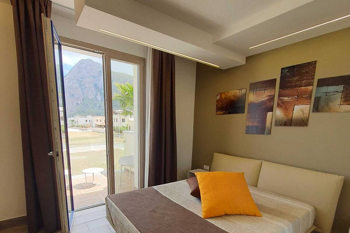 Quarto com cama, vista através de uma porta de vidro e montanha ao fundo.