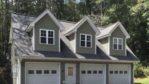 Une maison à deux étages avec un toit à pignon, deux portes de garage et une porte d’entrée.
