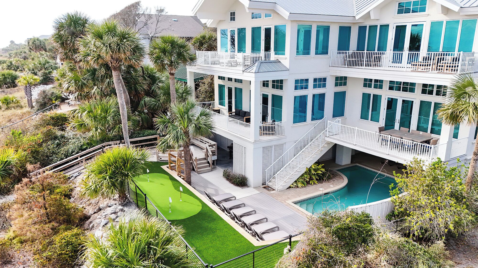 A multi-story house with a pool, a patio with chairs, and a small lawn.