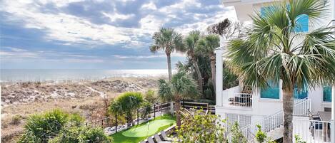 A coastal property with a golf course, a white building with blue windows, and a view of the beach.