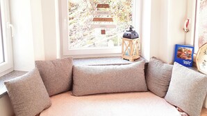 A cozy seating area with a cushioned bench, a decorative star hanging above, and a view of a garden through a window. - Ferienhaus Kaiserblick 125 qm für Max. 6 Personen und 3 Hunde (Kiefersfelden)