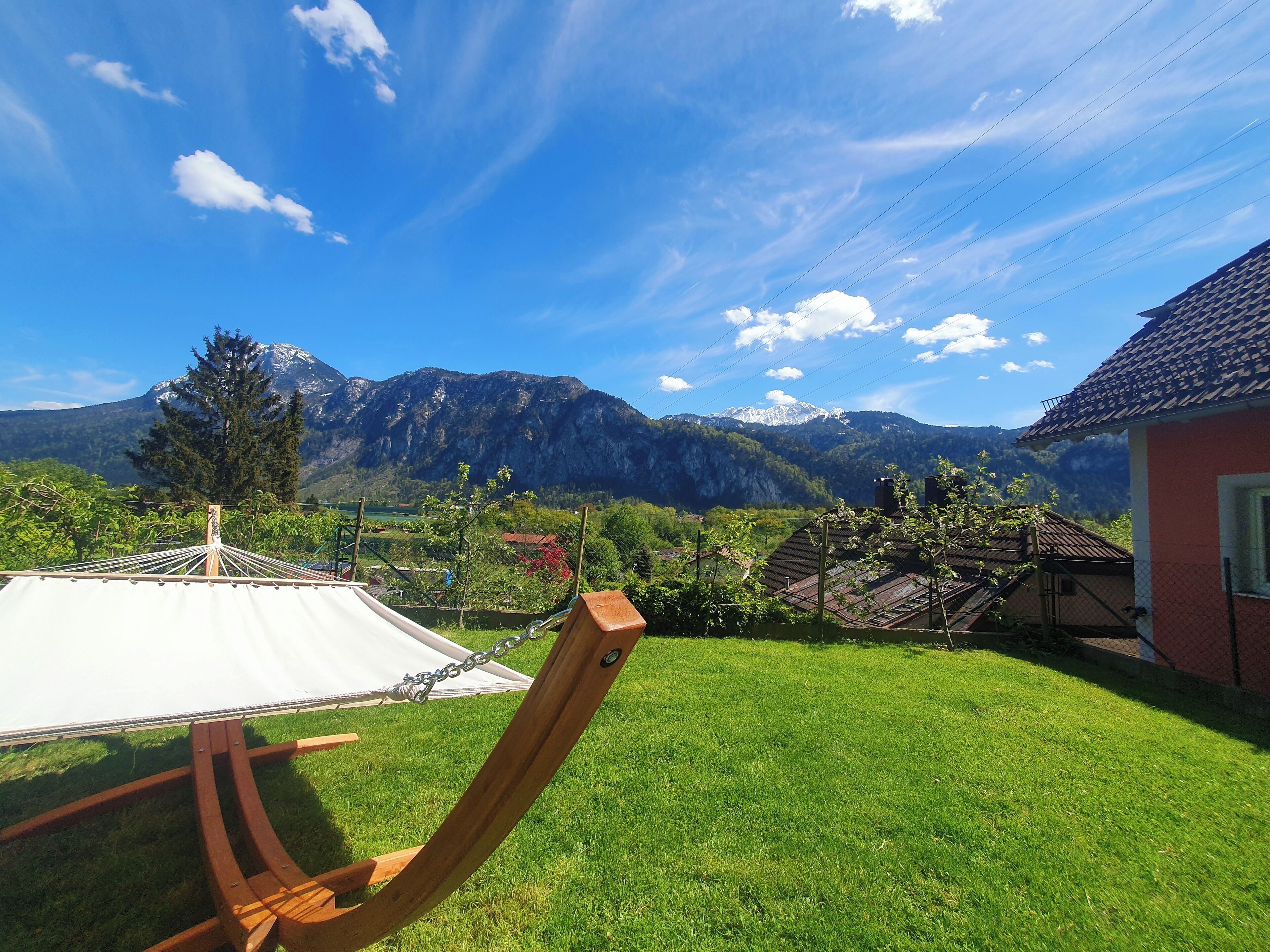 A grassy yard with a hammock and a white umbrella, a red building, and a mountain range in the background.