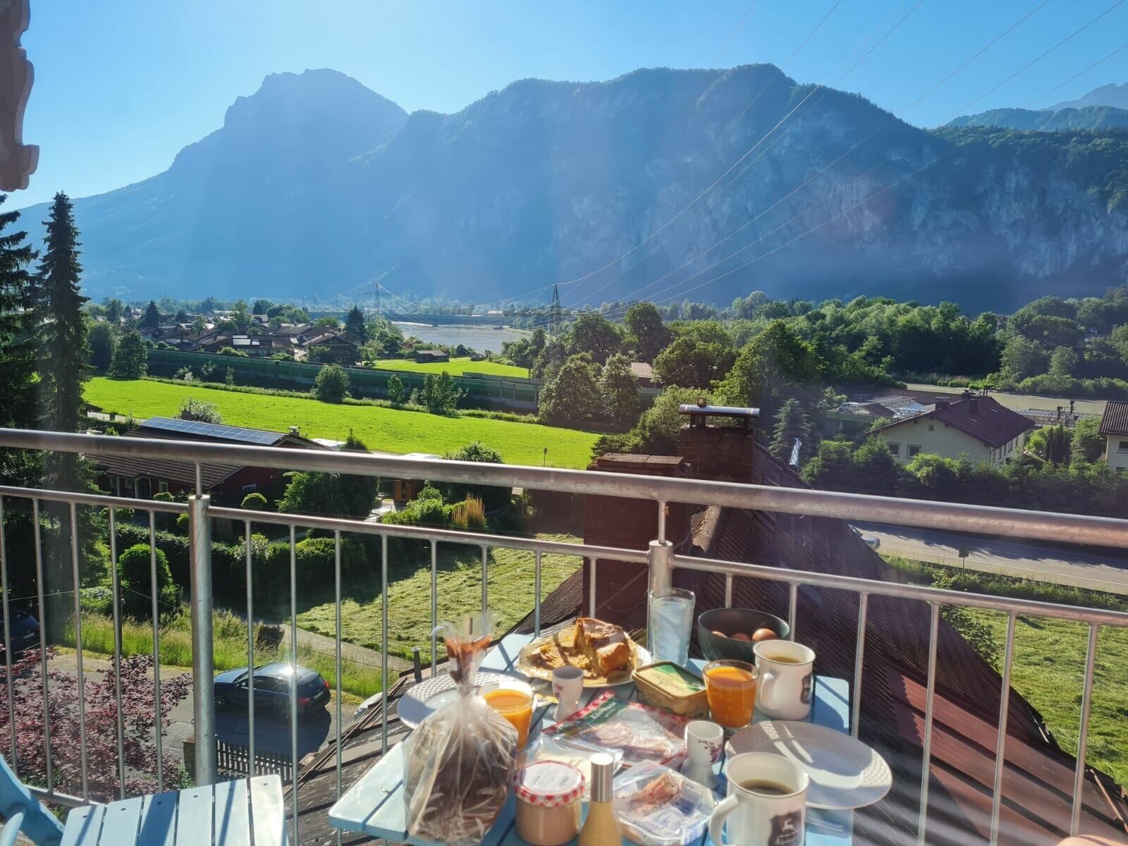A balcony with a table set for breakfast overlooking a mountainous landscape.