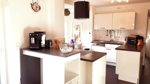 A modern kitchen with white cabinets, a coffee machine, and a hanging light fixture. - Ferienhaus Kaiserblick 125 qm für Max. 6 Personen und 3 Hunde (Kiefersfelden)