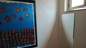 Ein kleines Zimmer mit einem Bett, einem gerahmten Kunstwerk an der Wand und einem Fenster.