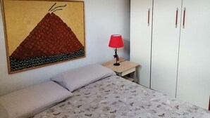 Ein Schlafzimmer mit einem Bett, einem Nachttisch mit Lampe, einem Kleiderschrank und einem Wandbild.