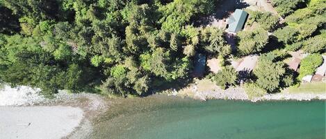 An aerial view of a coastal area with dense forest, a clear beach, and a small building near the shore.