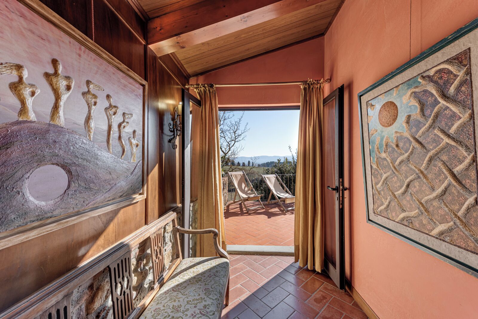 A hallway with a view of outdoor seating and a painting on the wall.