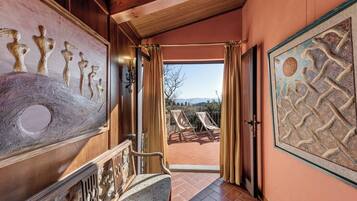 A hallway with a view of outdoor seating and a painting on the wall.