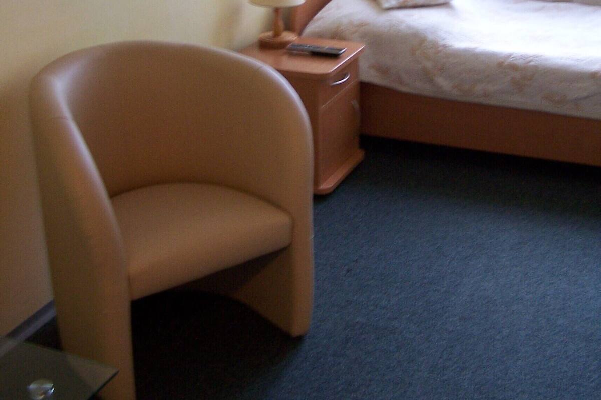 A hotel room with a single bed, a chair, a bedside table with a lamp, and a small table with a remote control.