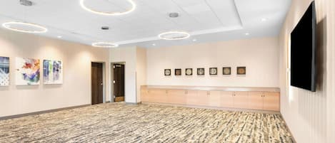 A spacious lobby with a patterned carpet, recessed lighting, a long reception desk, and framed artwork on the walls.
