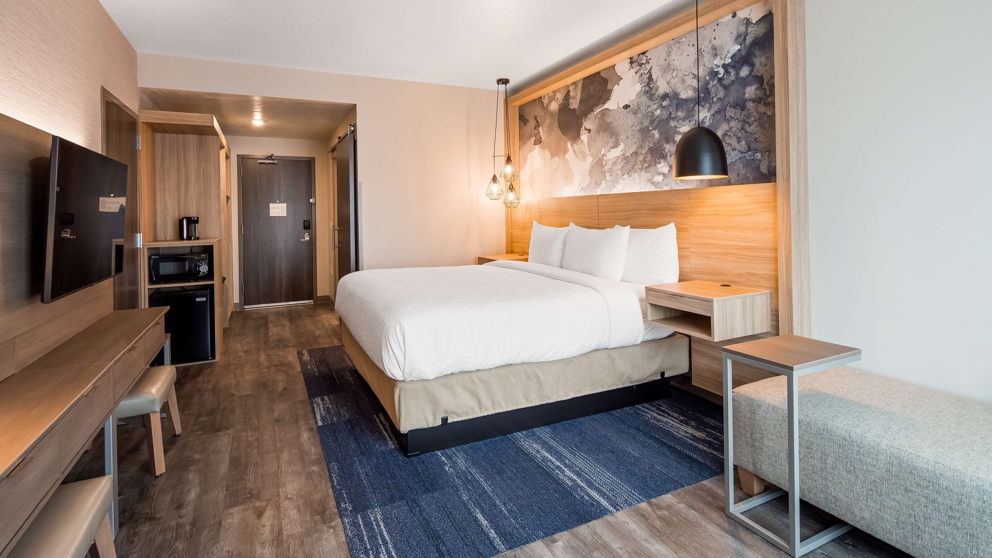 A modern hotel room with a large bed, a desk, a flat-screen TV, a microwave, and a coffee maker.