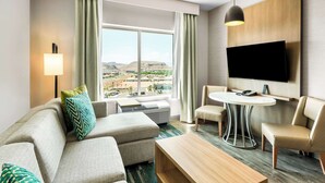 Una habitación de hotel moderna con un ventanal grande, un televisor de pantalla plana, un sofá, una mesa de centro y una mesa de comedor.