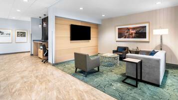 A modern lobby with a grey sofa, a small round table, and a flat-screen TV mounted on the wall.